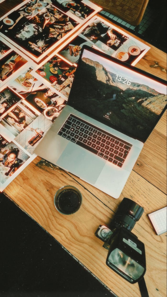 our-story Flat lay of a creative workspace with a laptop, camera, and printed photographs.