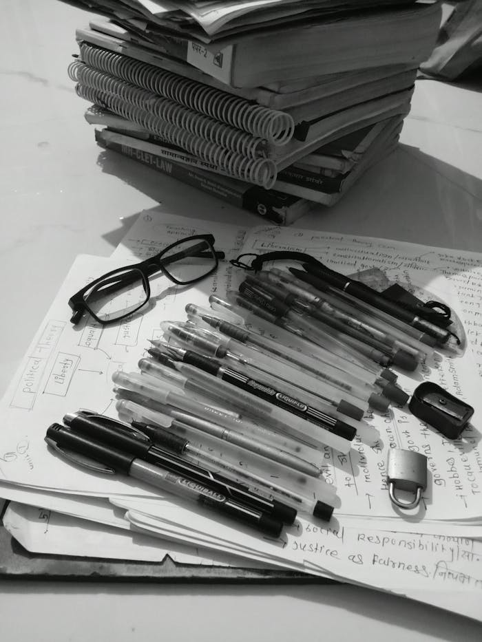 Black and white study desk with books, pens, glasses, and notes.