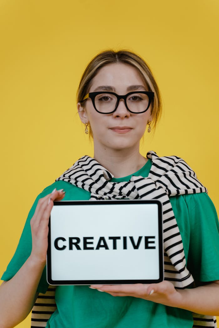 creative-03 Young woman holding a tablet displaying 'Creative' on a yellow background.